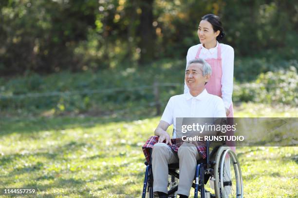 caregiver pushing senior man in wheelchair - 介護施設 ストックフォトと画像