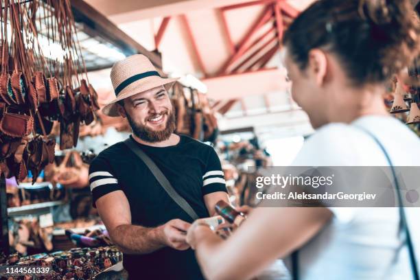 salesman successfully selling leather bag to female tourist - t shirtvendor stock pictures, royalty-free photos & images