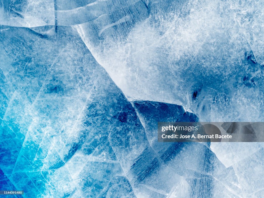 Full frame of the textures formed of a block of cracked ice on a blue and white color background.