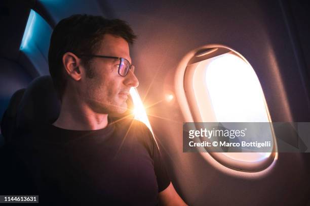 handsome man looking through airplane window during sunrise - inner views stock-fotos und bilder