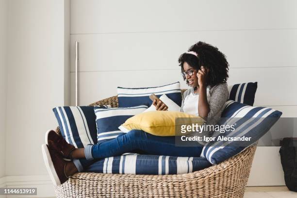 teenage girl resting listening to music on her mobile on the living room sofa - moving down to seated position stock pictures, royalty-free photos & images