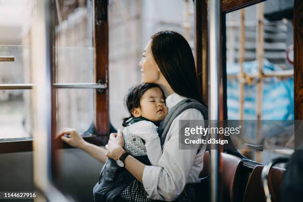 young asian mother with sleeping little daughter enjoying city scene through window while riding on city tram - mom resting stock pictures, royalty-free photos & images