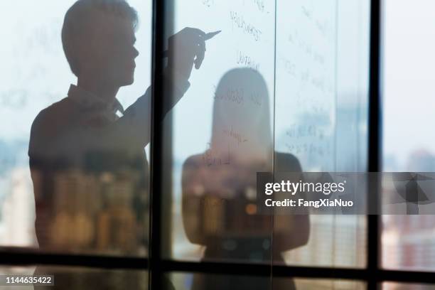 silhouette of man writing ideas on glass wall - business solutions silhouette stock pictures, royalty-free photos & images