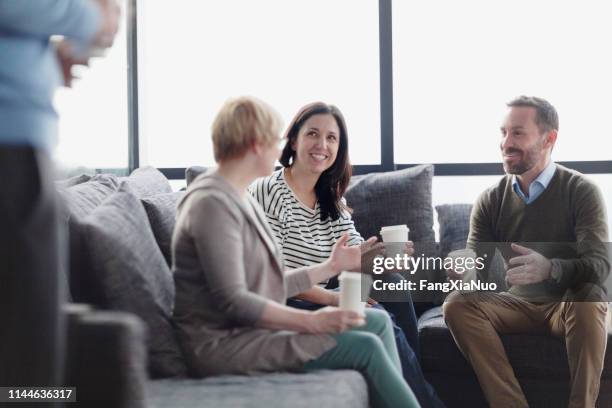 freunde sitzen auf der couch und teilen sich das gespräch - coffee break office stock-fotos und bilder