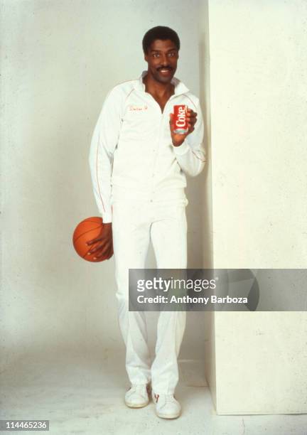 Portrait of American basketball player Julius Erving, aslo known as Dr. J as he poses with a can of Coca-Cola in one hand and a basketball in the...