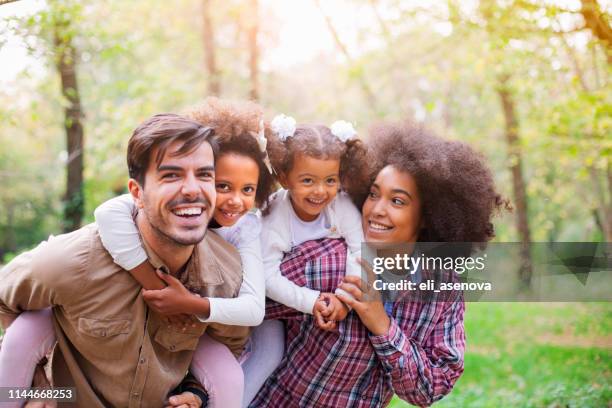 portrait of parents giving children piggybacks - diverse family stock pictures, royalty-free photos & images