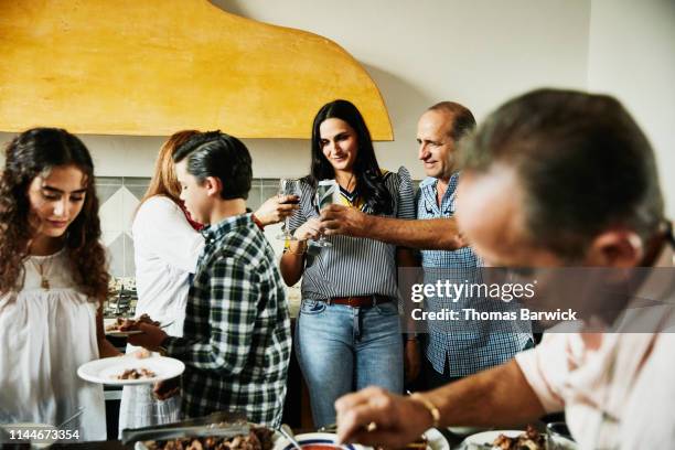 mature adults toasting in kitchen during multigenerational family dinner party - family choicepix stock pictures, royalty-free photos & images