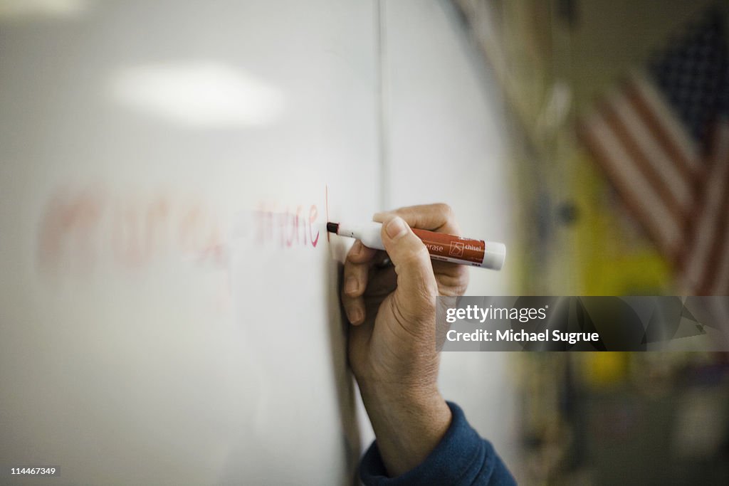 A hand holding a marker, writing on a board.