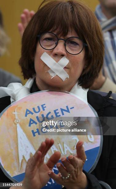 May 2019, Baden-Wuerttemberg, Ulm: A woman with a plaster over her mouth and a sign with the inscription "Auf Augenhöhe in unserer Kirche 0" stands...