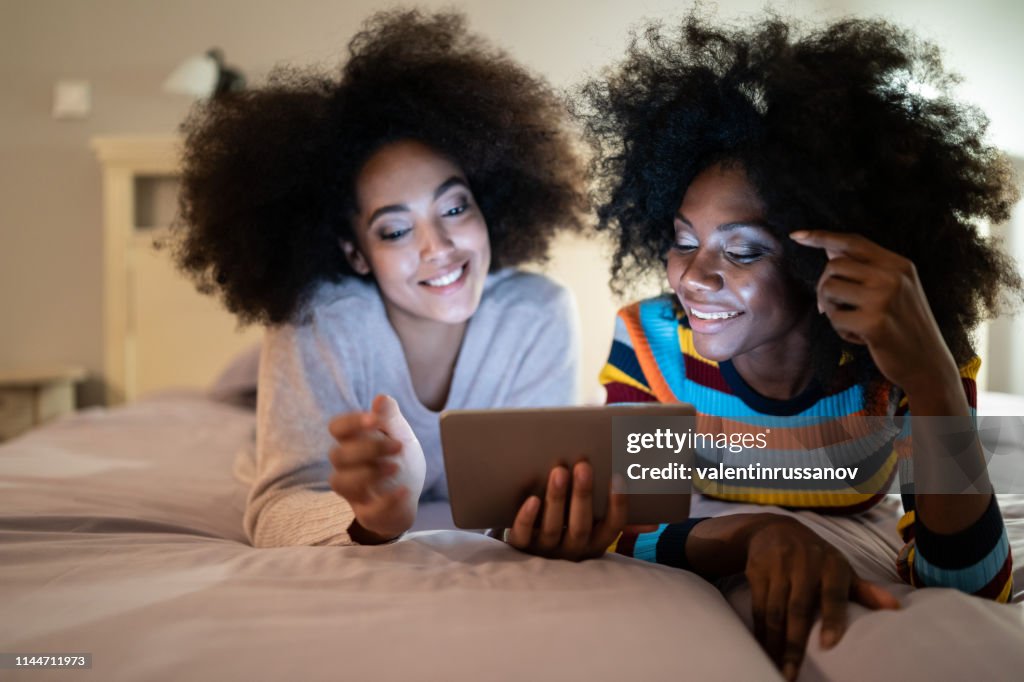 Friends using digital tablet in bed