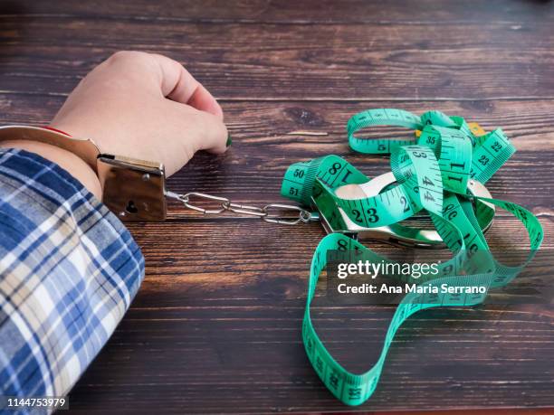 a person handcuffed with a tape measure. diet concept - bulimie stock-fotos und bilder