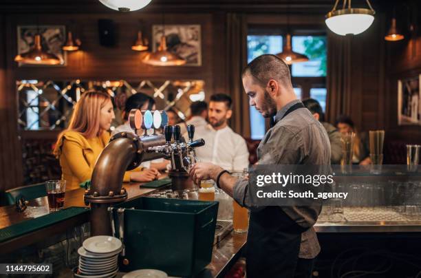 bartender pouring beer for customers in pub - bartender stock pictures, royalty-free photos & images