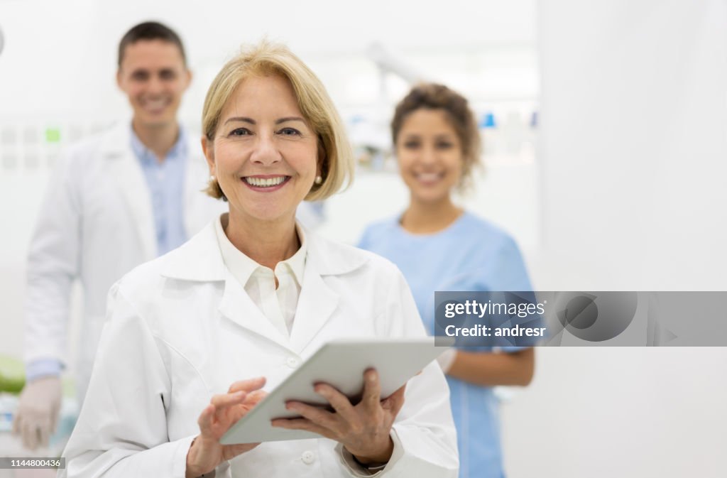 Happy dentist at the office with her team and holding a tablet computer