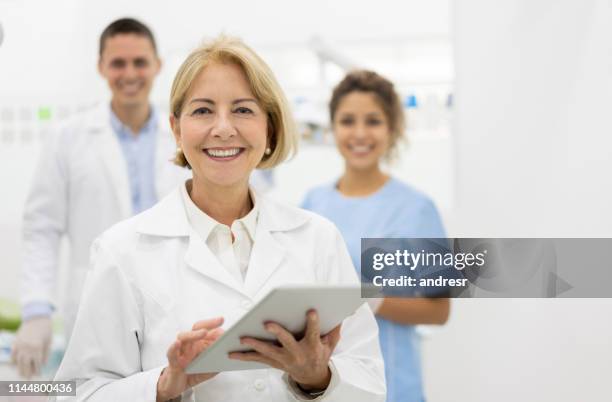 happy dentist at the office with her team and holding a tablet computer - dental health imagens e fotografias de stock