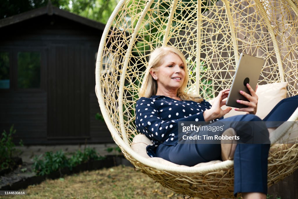 Woman using tablet on swing seat in garden