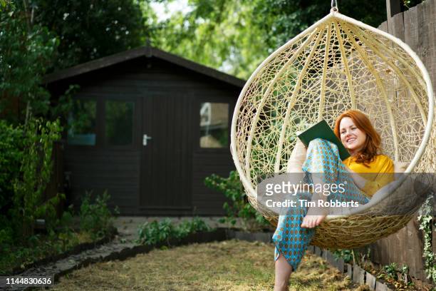woman reading book on garden swing seat - hanging in garden stock-fotos und bilder