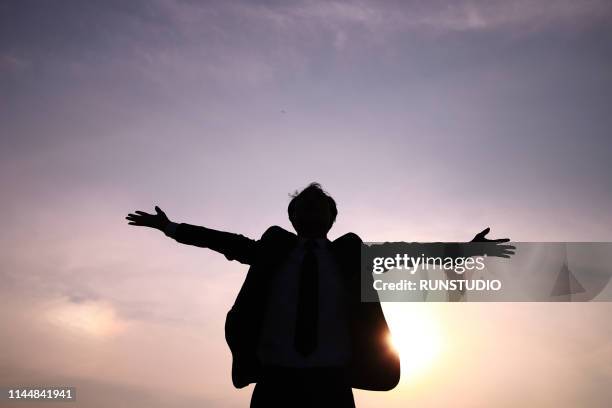 silhouette businessman stretching arms against sky at sunset - 解放 ストックフォトと画像