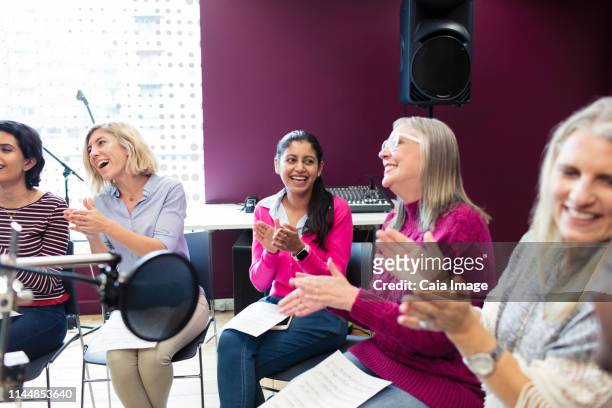happy womens choir with sheet music singing and clapping in music recording studio - choir uk stockfoto's en -beelden