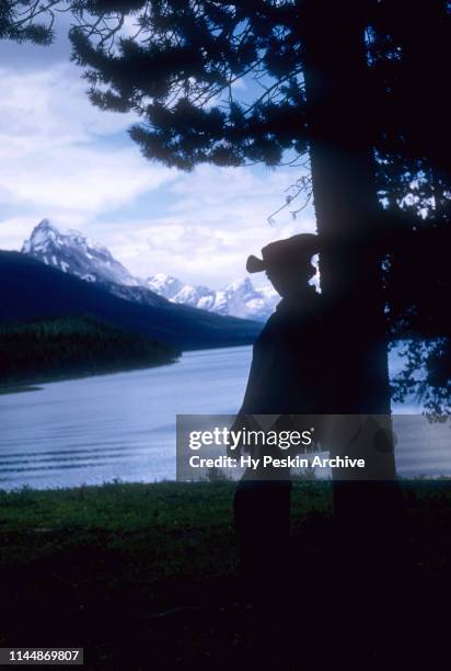 General view of a silhouetted woman resting and gazing at the lake while adventuring through the Jasper Trail on horseback circa July, 1954 in...