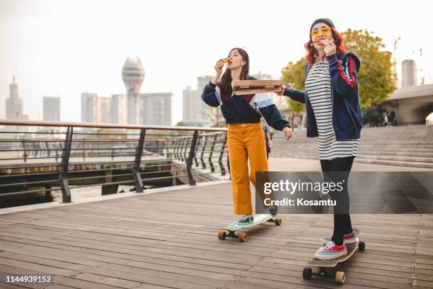 mujeres hipster comiendo pizza y montando tablas largas - asian teenager fotografías e imágenes de stock