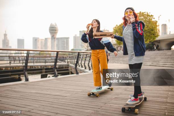 hipster women eating pizza and riding long boards - longboard surfing stock pictures, royalty-free photos & images