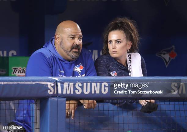 Assistant athletic trainer Jose Ministral and head athletic trainer Nikki Huffman of the Toronto Blue Jays look on from the dugout during MLB game...