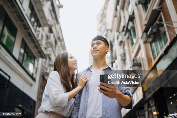 junges asiatisches ehepaar spaziert entlang der stadtstraße plaudert und lächelt beim smartphone - central asia stock-fotos und bilder