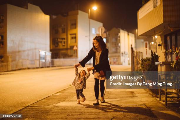 pretty young mom strolling with lovely little toddler hand in hand joyfully at night. - mother and daughter on night street stockfoto's en -beelden