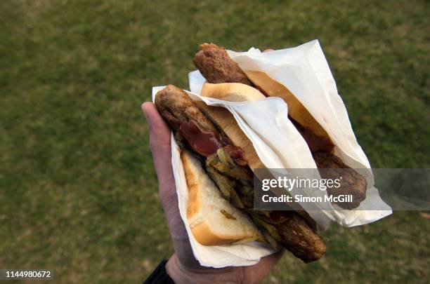 sausage sizzle sandwiches with fried onion and bbq sauce in a white paper napkin held in a man's hand in a park - fried stock pictures, royalty-free photos & images