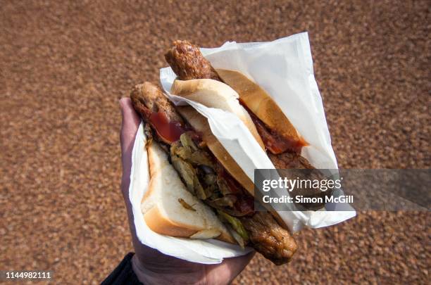 sausage sizzle sandwiches with fried onion and bbq sauce in a white paper napkin held in a man's hand in a park - democracy sausage stock pictures, royalty-free photos & images