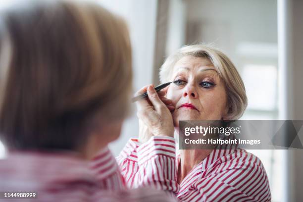 a rear view of active senior woman applying make-up at home, looking in the mirror. - eye liner stock pictures, royalty-free photos & images