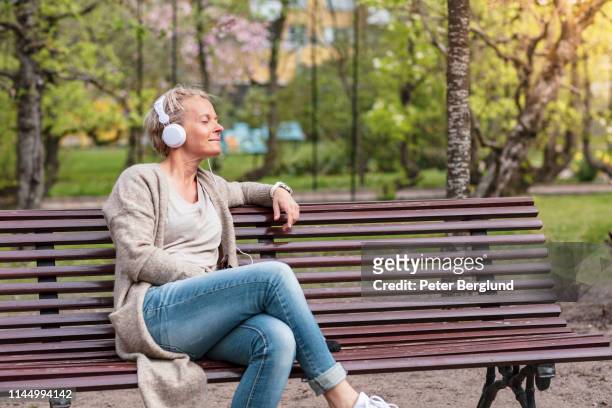 woman listening to music in a park - 50 54 years stock pictures, royalty-free photos & images