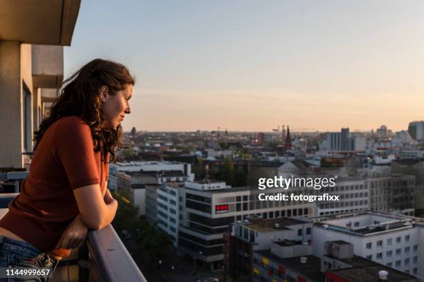 porträt der jungen frau lehnt sich auf balkon und blickt bei sonnenuntergang auf die skyline von berlin - berlin stock-fotos und bilder