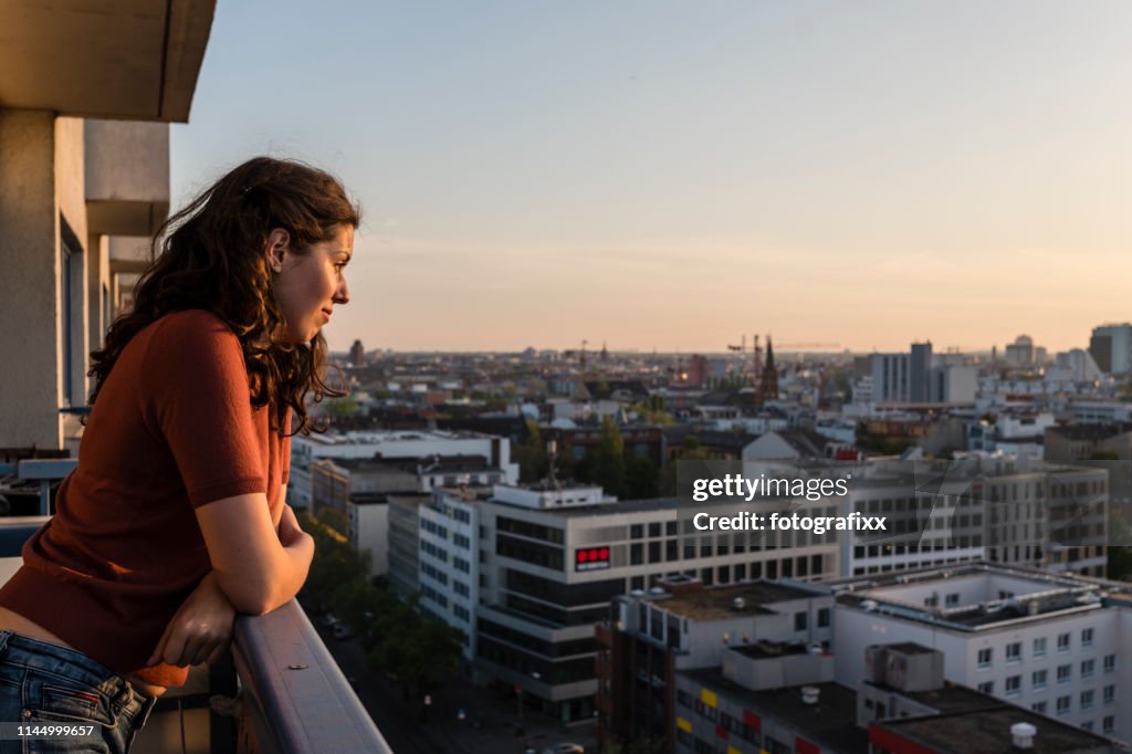 Porträtt av ung kvinna lutar på balkongen och ser över Berlins skyline medan solnedgången