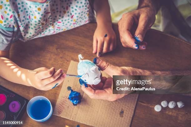 padre e hijo pintando arcilla hecha a mano little piggy bank - manos pintadas fotografías e imágenes de stock