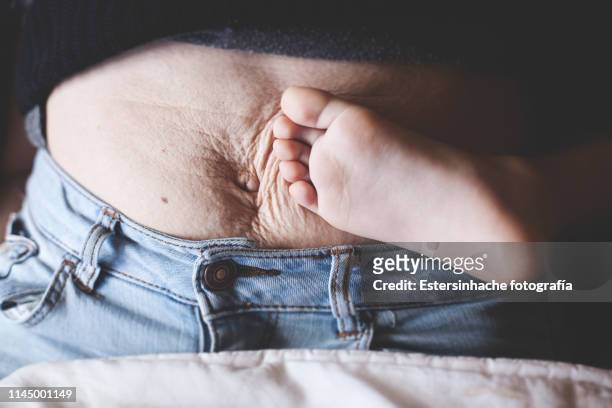 photograph of a woman's belly after giving birth, next to the barefoot of her son - pregnant belly stockfoto's en -beelden