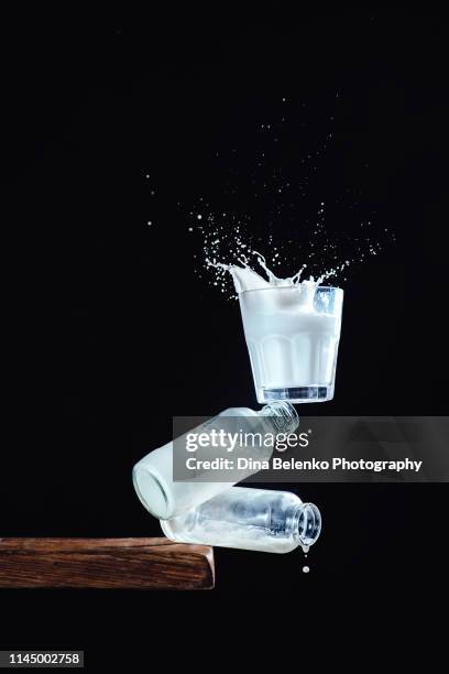 glass of milk with a splash balancing on milk bottles on an edge of a table. half full, half empty. conceptual still life photography with copy space - half complete stock pictures, royalty-free photos & images