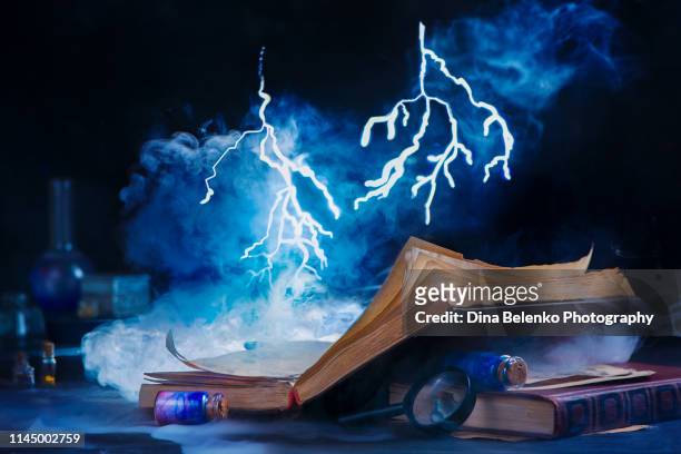 an open book with tiny lightning above it. magical spellbook of weather forecasting. dark conceptual still life with copy space - wicca stock-fotos und bilder