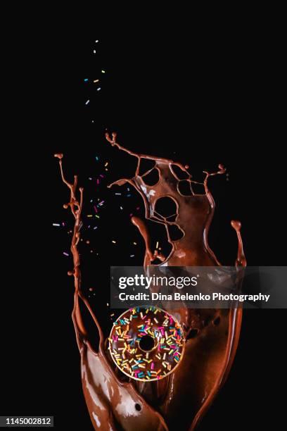 chocolate splash and a donut with chocolate glazing on a dark background with copy space. high-speed action food photography. - black room stockfoto's en -beelden