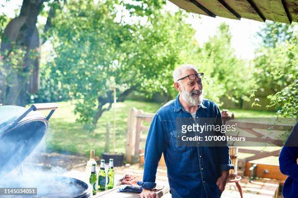 cheerful mature man smiling by bbq in garden - mature men stock pictures, royalty-free photos & images