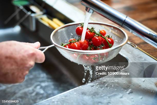 cherry vine tomatoes being washed in sieve - food waste stockfoto's en -beelden
