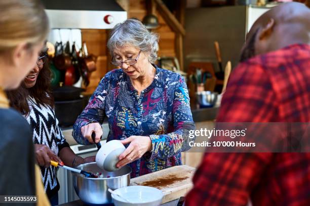 senior woman making food with multi racial friends - cooking demo stockfoto's en -beelden