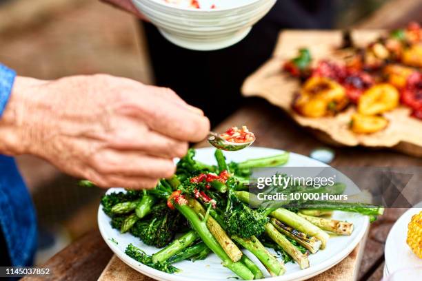 person spooning sauce over freshly cooked green vegetable medley - mediterranean food fotografías e imágenes de stock