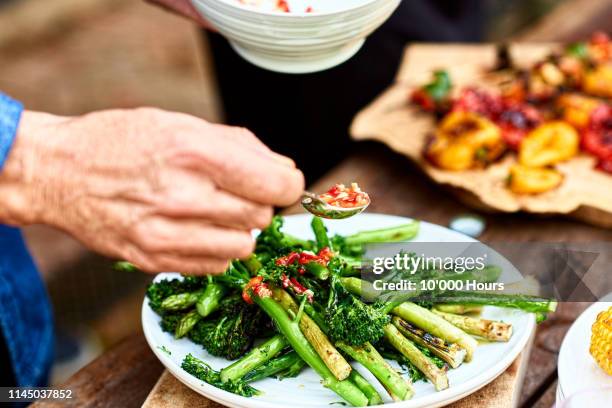 person spooning sauce over freshly cooked green vegetable medley - barbecue cibo foto e immagini stock