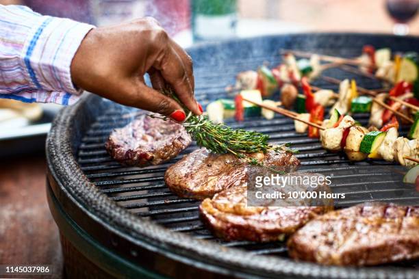 woman basting meat on barbecue with fresh herbs - gegrillt stock-fotos und bilder