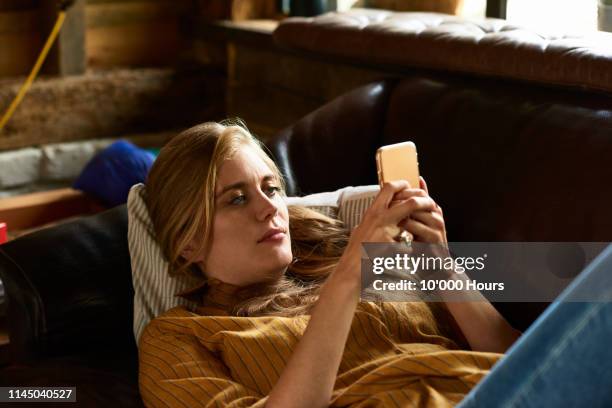 portrait of woman concentrating on phone reclining on couch - sofa stock-fotos und bilder