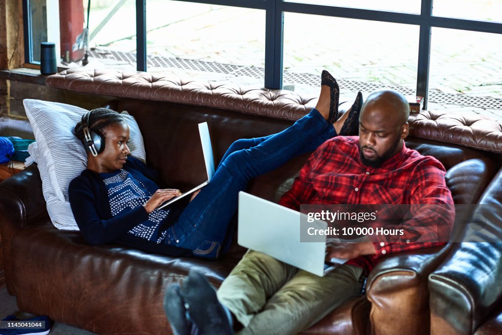 Couple sitting on sofa using laptops and relaxing