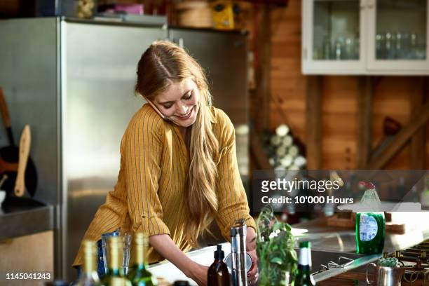 attractive woman using phone and doing dishes - woman cooking phone stock-fotos und bilder