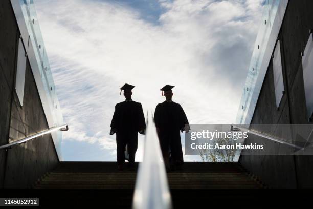 silhouette of two college graduates climbing steps - post secondary education stock pictures, royalty-free photos & images