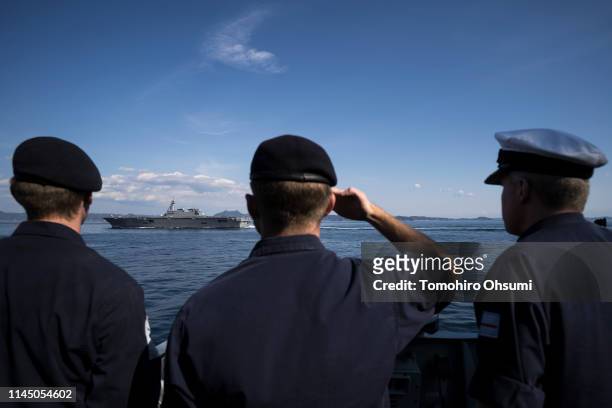 Members of the British Royal Navy look at Japanese Maritime Self-Defense Force's Izumo helicopter carrier on board the HMS Montrose frigate as it...